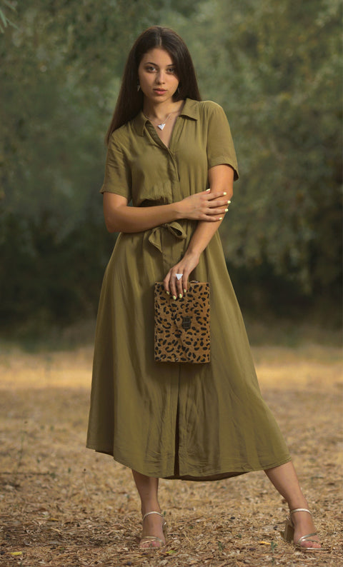 Woman in a green dress holding a leopard print clutch in a natural setting