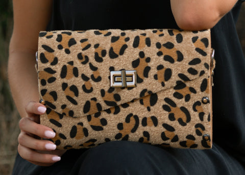 Leopard print clutch held by a person against a dark background