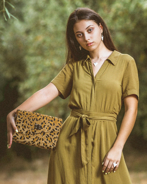 Woman in a green dress holding a leopard print clutch against a blurred natural background