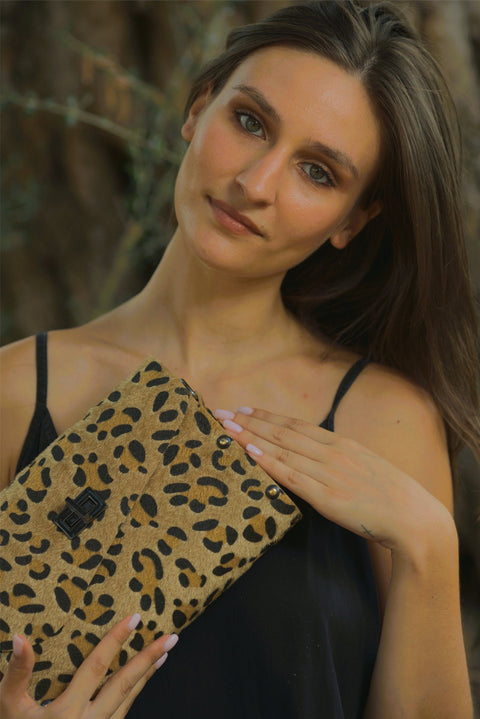 Woman holding a leopard print clutch against a blurred natural background
