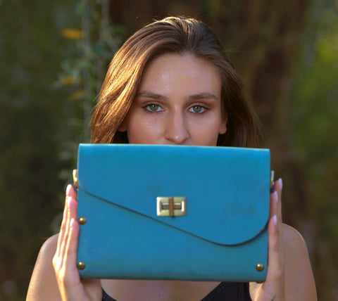 Woman holding a blue clutch in front of her face with a blurred natural background