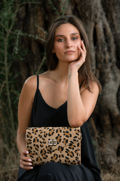 Woman holding a leopard print clutch against a natural background