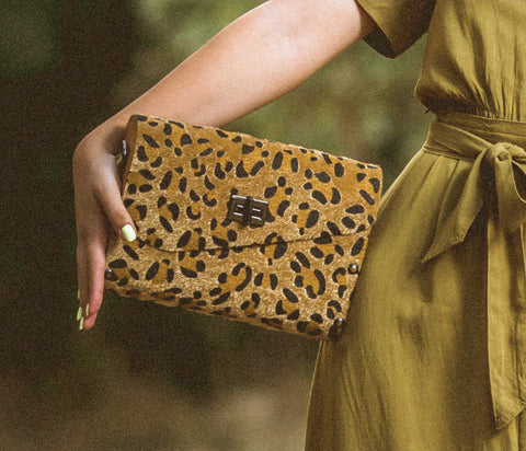 Person holding a leopard print clutch bag with a blurred natural background